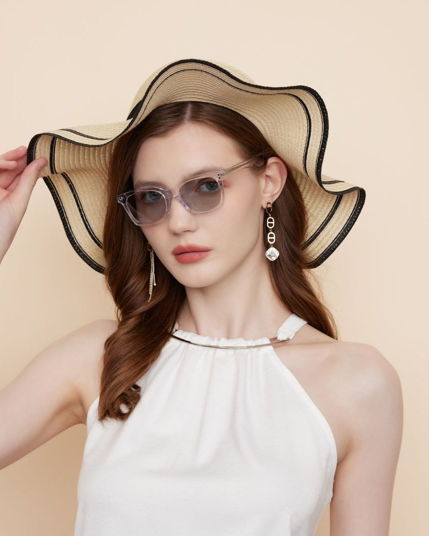 A woman in a straw hat wearing clear acetate frames against a sand backdrop